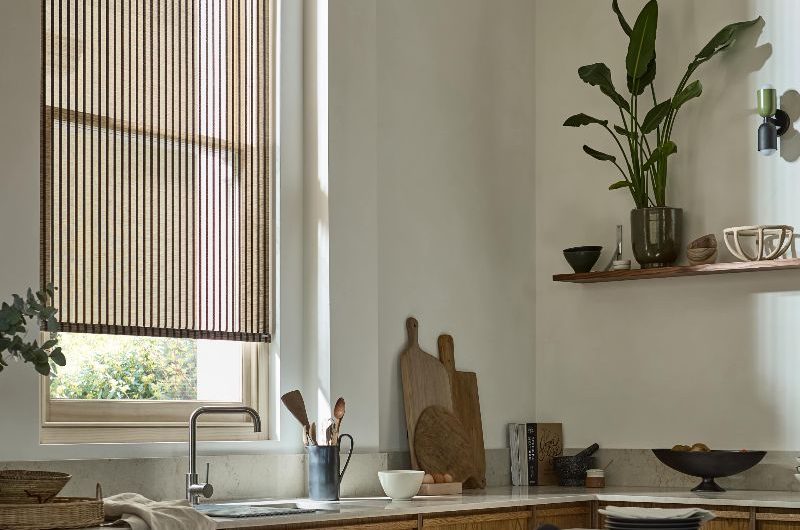 A modern rustic kitchen with wood cabinetry, striped roller blind, and an island with two bar stools.