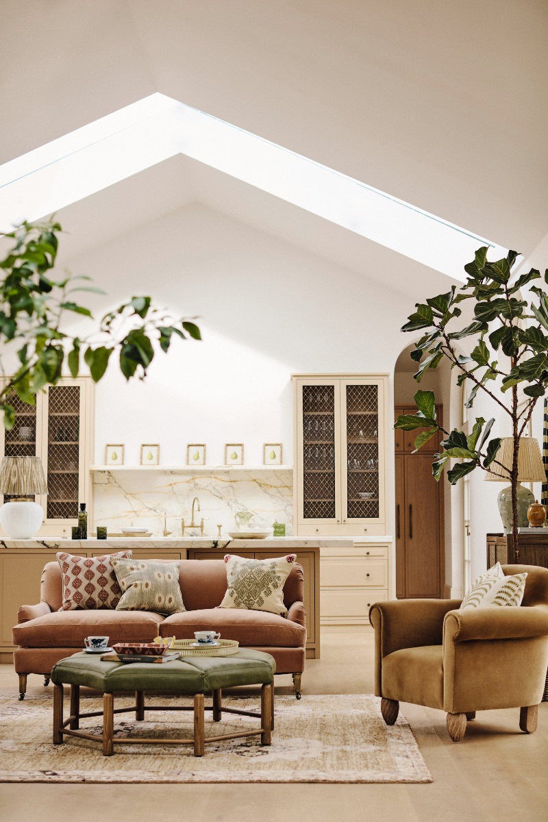 A spring kitchen-living room with velvet sofa and armchair, neutral kitchen cabinetry, and skylights.
