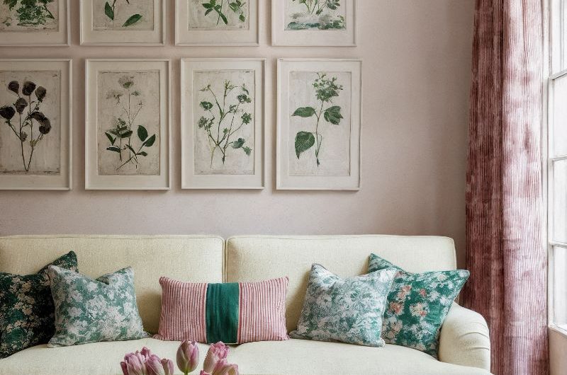 A spring living room with pink wall paint, floral art work, neutral two-seater sofa, and a green coffee table.