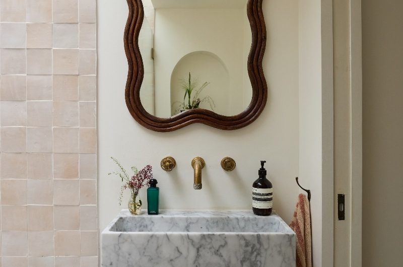 A vanity area with a marble basin, rattan mirror, next to a fitted tub.