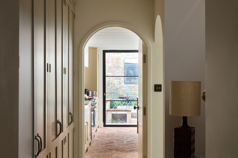 Bespoke cabinetry beside the staircase and a curved entryway to the kitchen.