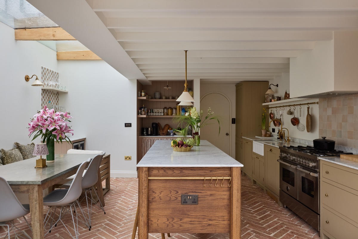 A calm kitchen design with exposed rafters, herringbone terracotta floor tiles, timber grain and brass hardware.
