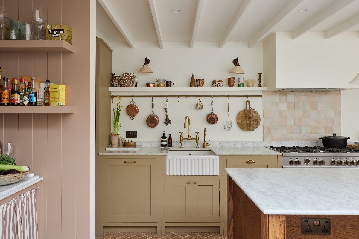 View of the kitchen's sink zone with neutral cabinetry, a fluted butler sink, brass tap, brass rail and open shelf.