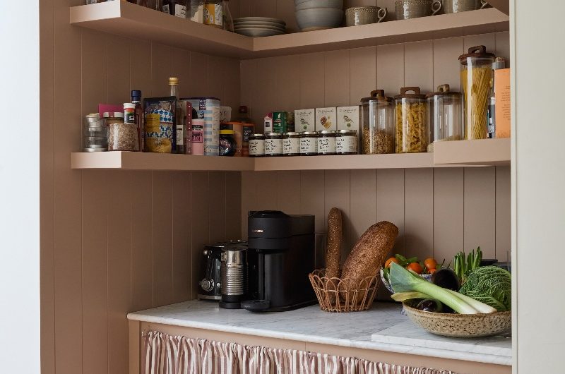 An open kitchen pantry with open shelves, a curtain skirt, and panelling.