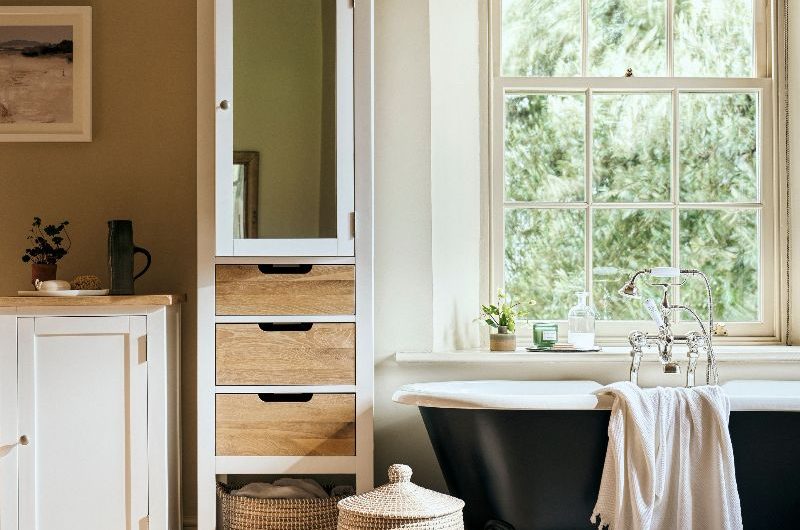 A modern rustic bathroom with a mix of furniture, a black painted roll top tub, and seagrass storage baskets.