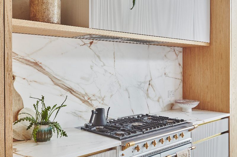 A bespoke timber and white reeded kitchen with a range cooker, and open shelving with house plants.