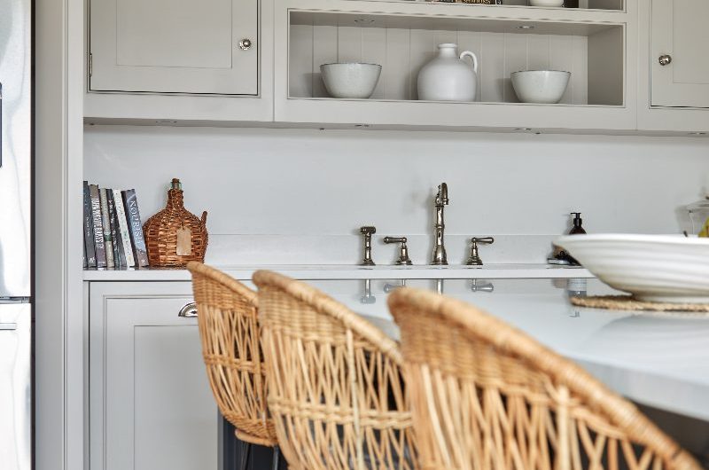 A coastal kitchen with off-white cabinetry, a dark blue island, and rattan bar stools.