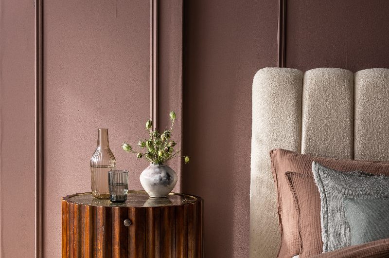 A calm bedroom with a scalloped headboard, classic wall panelling, and fluted wood bedside table.