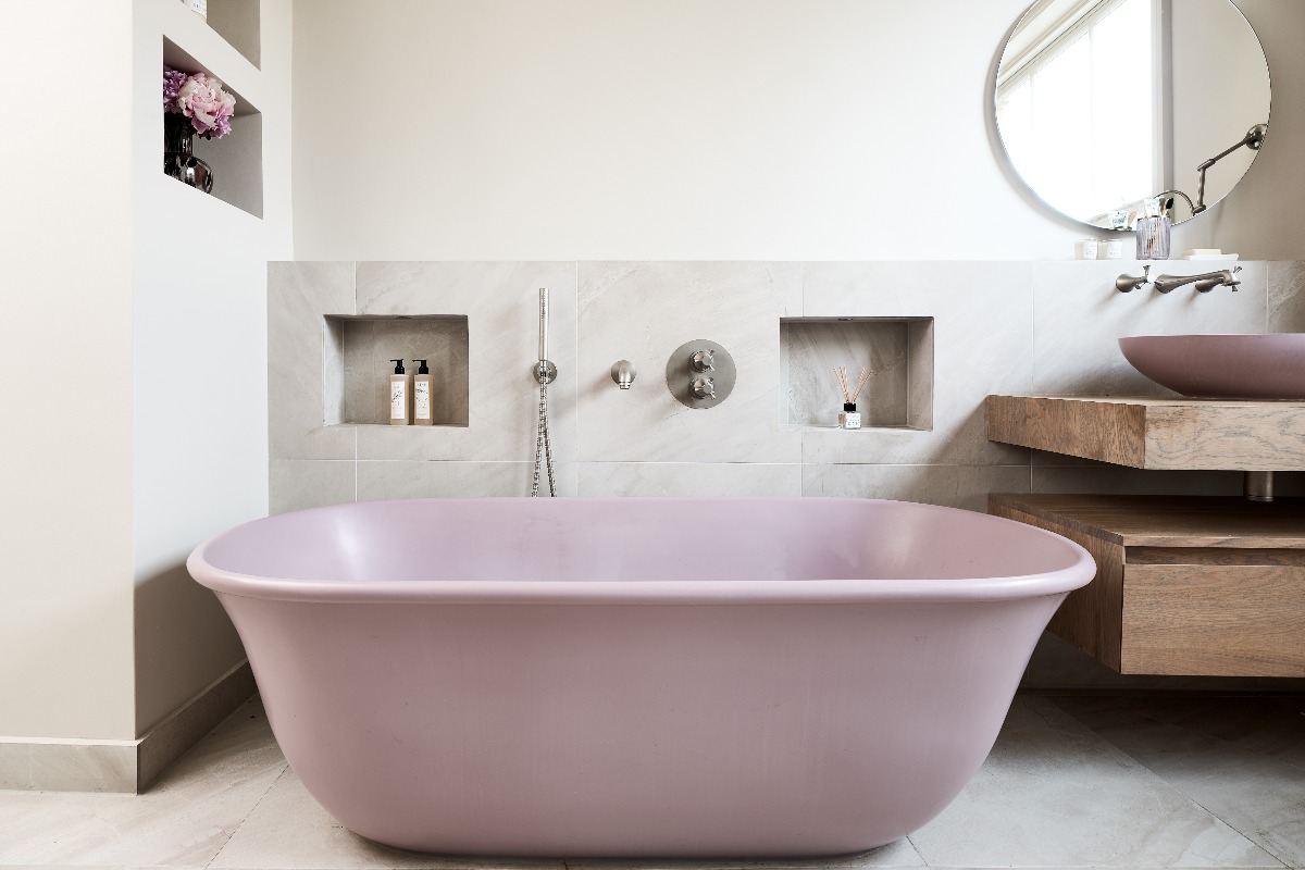 A bath zone with a pink tub, built-in storage and natural stone-effect tiles.