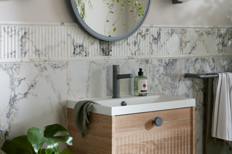 A modern bathroom with fluted marble wall tiles, a tactile wood vanity, an LED mirror and coloured brassware.