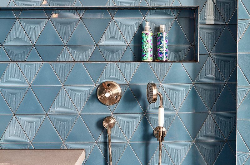 A vibrant blue, tiled bathroom with a handy niche next to the bath.
