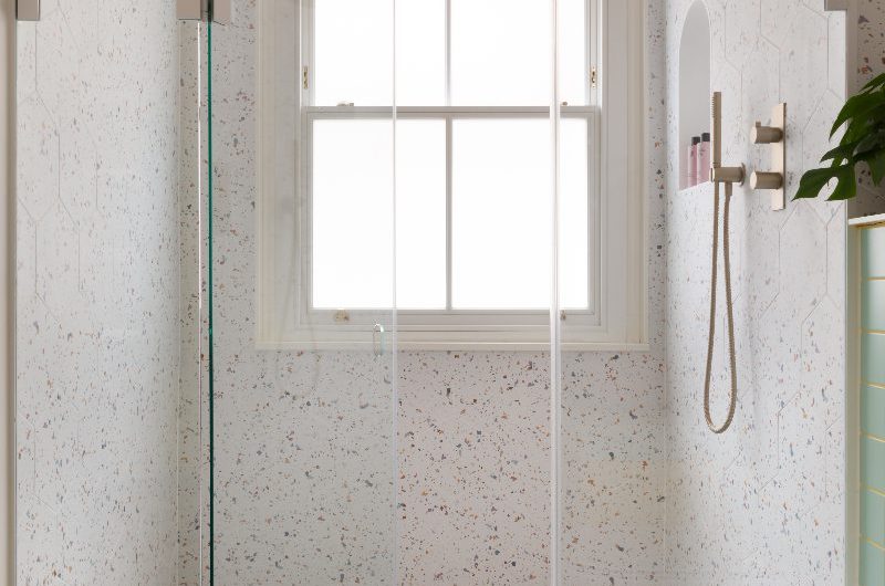 A modern design with a speckled shower with gold brassware and a storage niche.