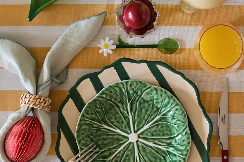A colourful Easter table with a yellow and white striped tablecloth, striped plate and cabbage-shaped bowl, with pea-shaped salt and pepper shakers.