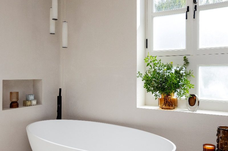 A zen bathroom with a freestanding tub, textured wall and floor coverings, and matt black accents.