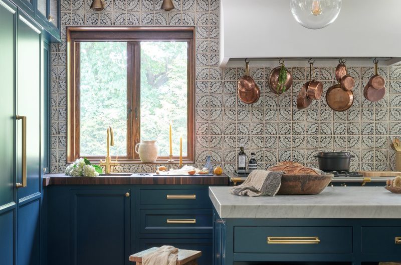 View of the sink area with dark blue cabinetry and handmade splashback tiles, with a range cooker and plastered canopy next to it.