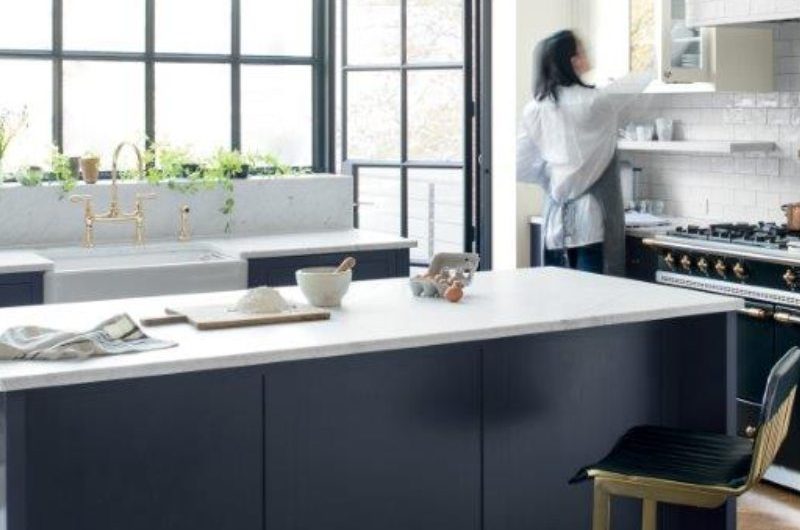 A classic scheme with a central, painted island with art deco chairs, dark wood flooring, and veiny marble worktops.