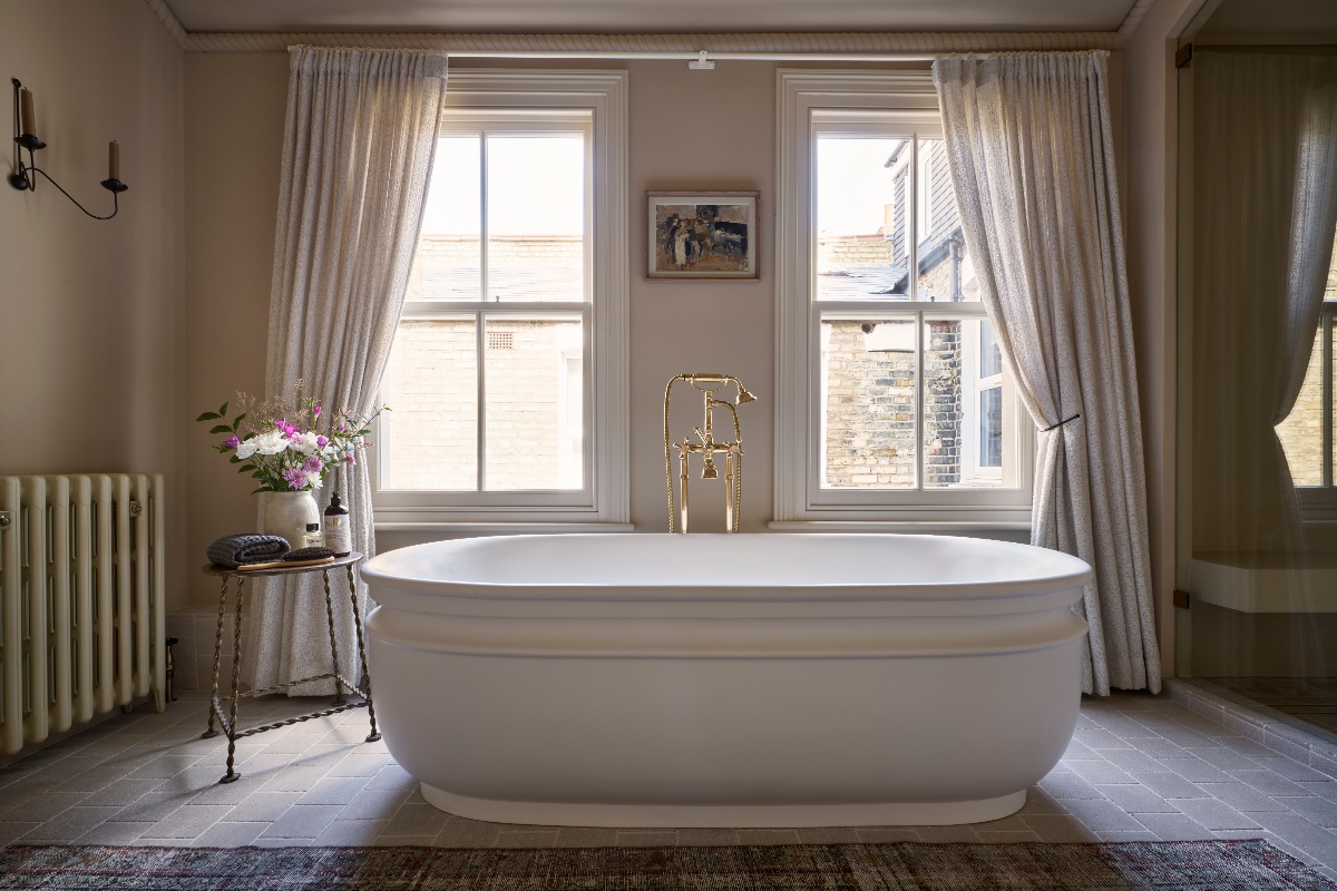 View of a luxurious bath with soft curves, a freestanding bath filler, and sash windows at the back.