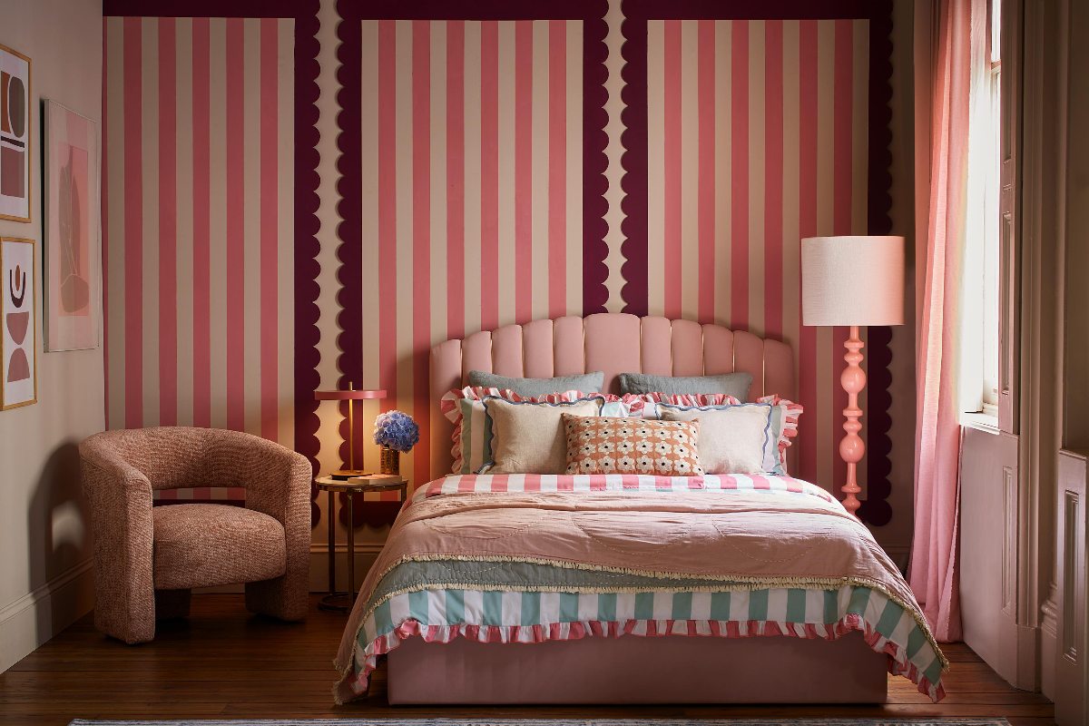 A modern bedroom with striped wall coverings, layered textiles, and a warm palette of pinks.