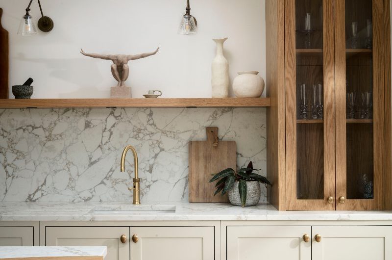 A calm design with neutral cabinetry, wood units and an open shelf, and marble surfaces.