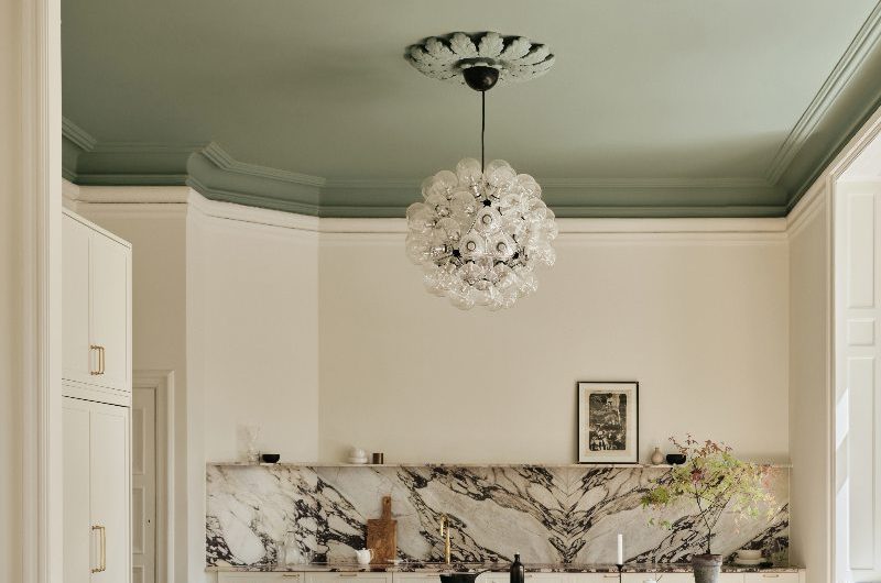 A light and bright kitchen design with a green ceiling, viola marble, and statement chandelier.