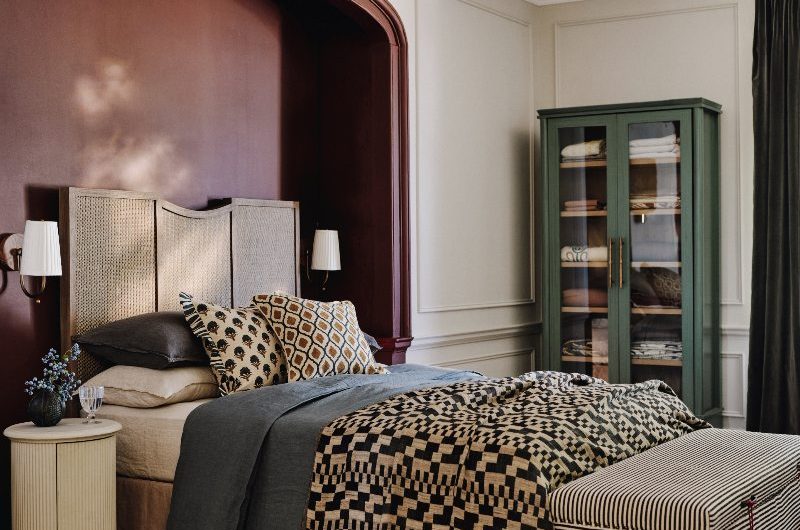 A modern scheme with a glazed glass cupboard, a statement bed, tactile furnishings, and a striped ottoman.