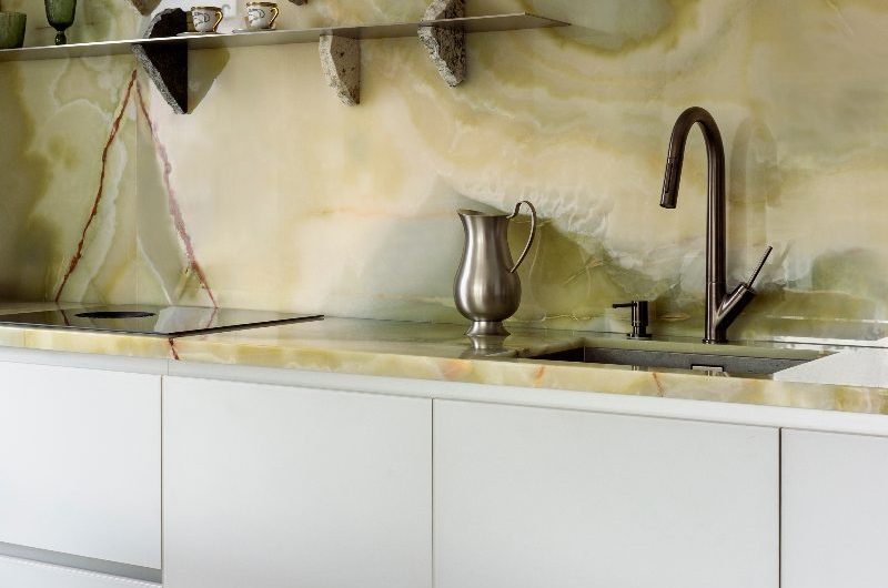 A wash up zone with a gunmetal tap, inset sink, green onyx stone surfaces and steel shelves.