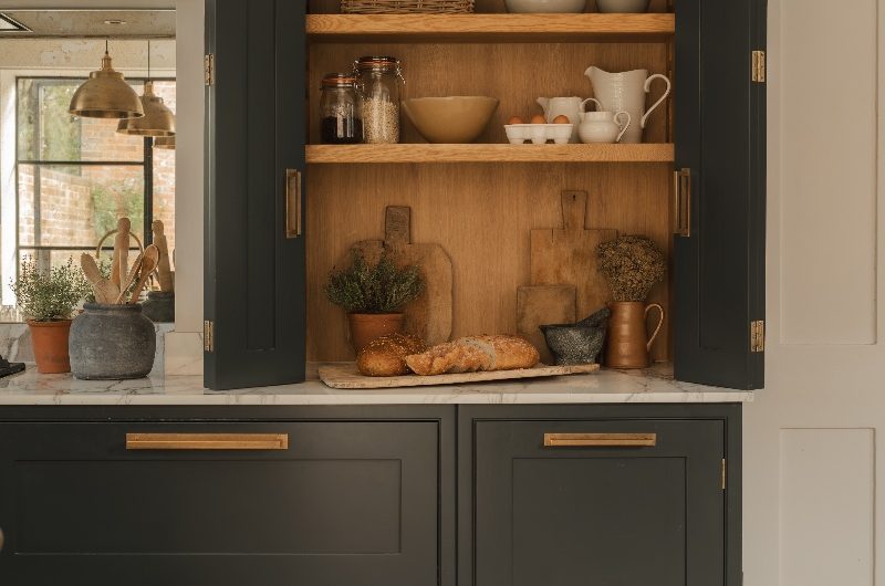 A breakfast cupboard with bi-fold doors in a black kitchen with marble surfaces.