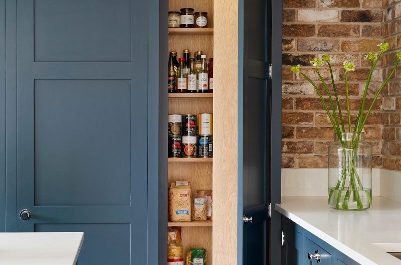 A dark blue shaker kitchen with chrome hardware, oak interiors, and white surfaces.