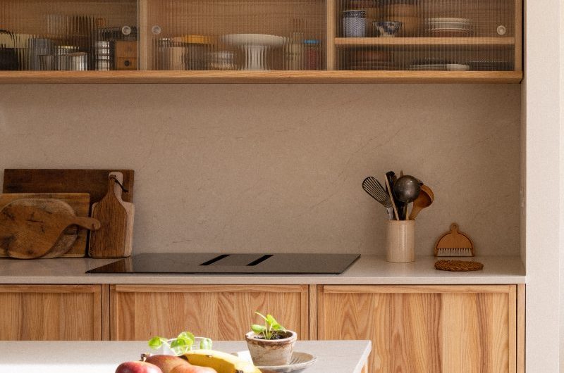 Closeup at grainy wood cabinets with neutral work surfaces, and fluted glass wall-mounted units.