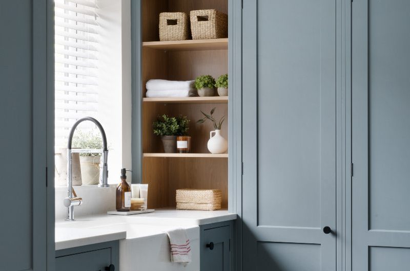 A utility room with light cabinets, a butler sink, chrome tap, and wood shelving.