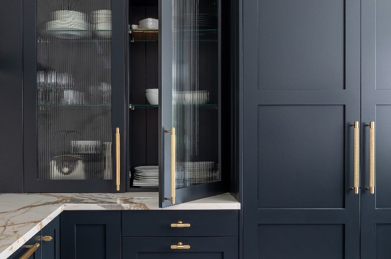 Blue shaker kitchen design with gold textured handles, fluted cabinets, and marble worktops.