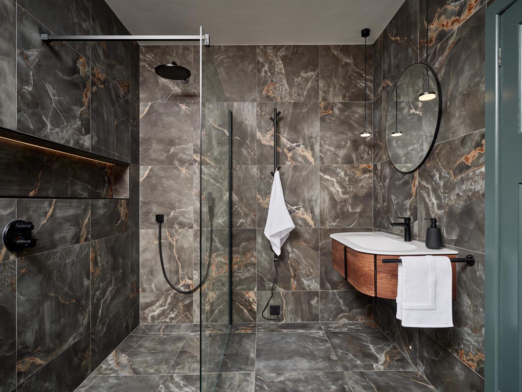A dramatic ensuite with floor-to-ceiling onyx-effect tiles, wood furniture, black hardware, and a shower area.