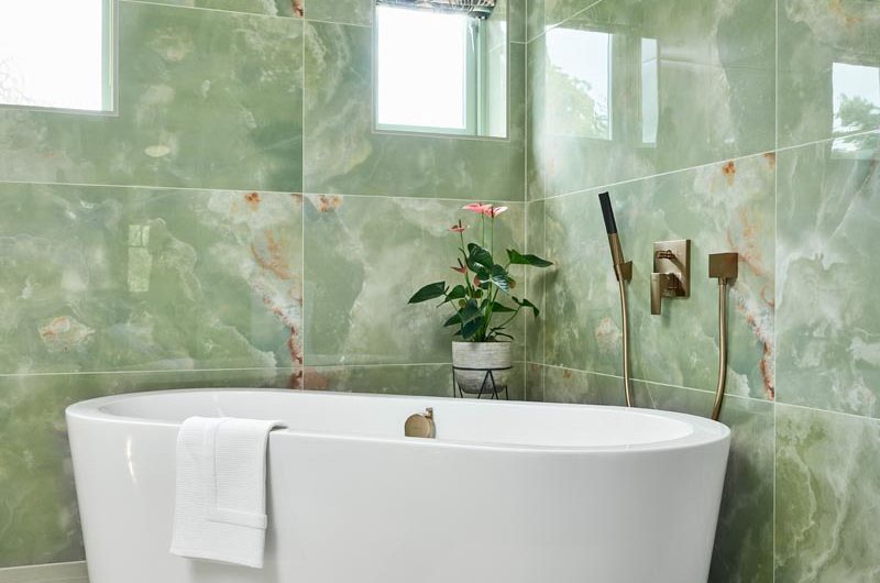 A light ensuite design with green onyx effect tiles, gold brassware and a freestanding bath.