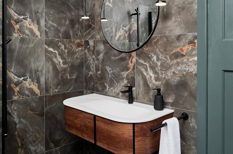 Vanity zone with wood wall-mounted unit, white basin, black tap and accessories, and a circular mirror above it.