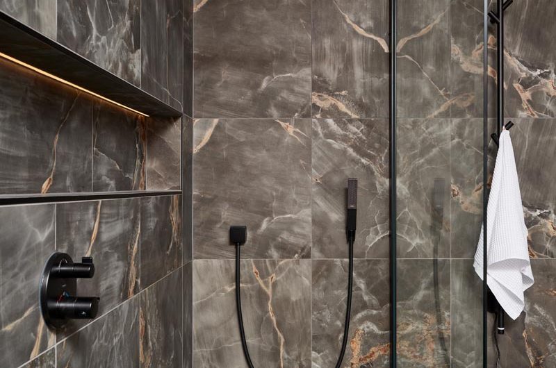 A dark ensuite design with dark onyx effect tiles, black brassware and an illuminated storage niche in the shower area.