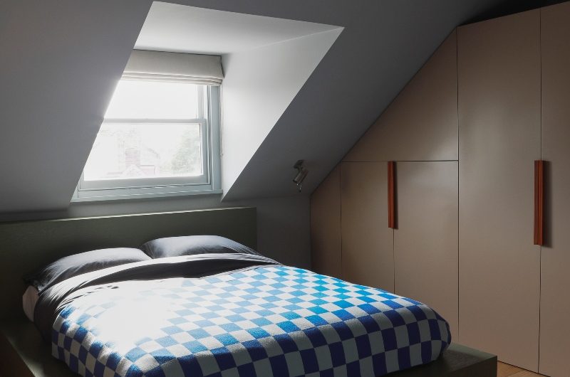A bedroom with custom-made cabinetry painted a neutral shade with a green bed frame under a sloped roof.