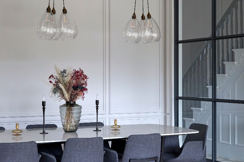 A formal dining area with a marble topped table, dark grey chairs, and wall panelling.