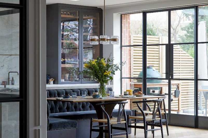 A kitchen design with an L-shaped island, steel-framed glazing and a mix of glass fronted and closed cabinetry.