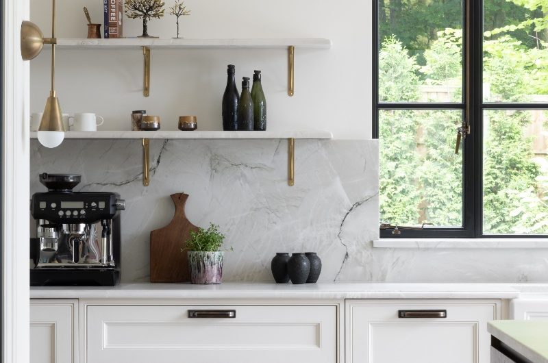 White cabinetry with sleek brass handles, veiny worktops and open shelving.