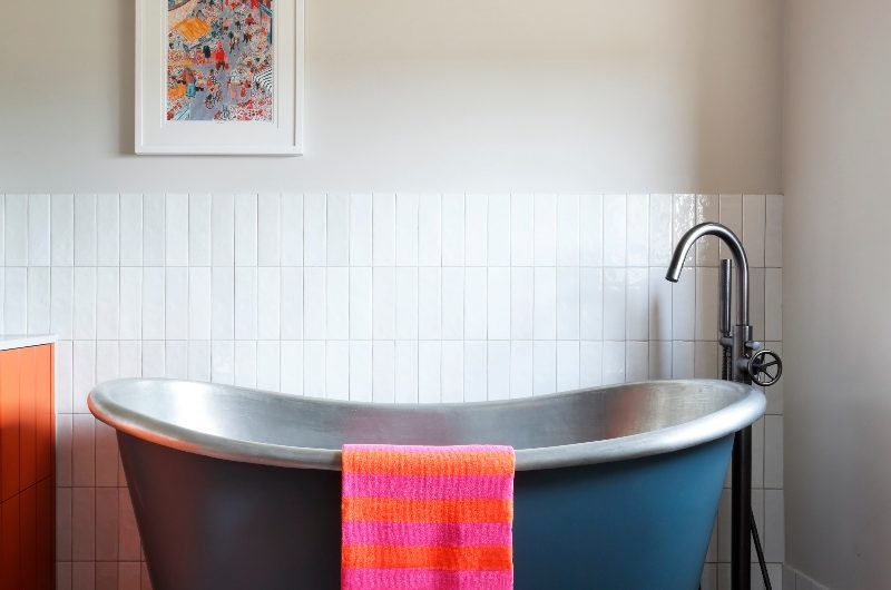Bathroom design with multicoloured tiles, a freestanding tub, gunmetal brassware and wall art.