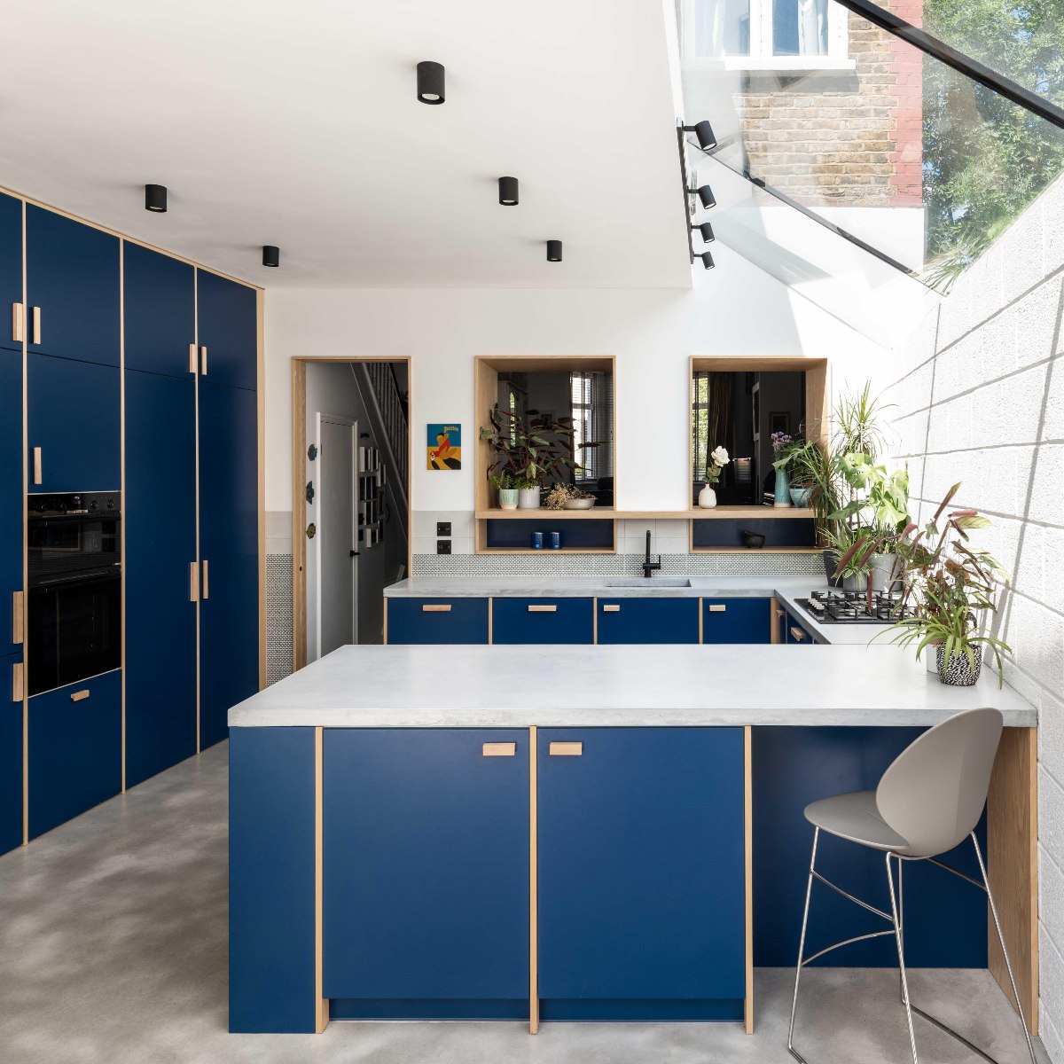 A U-shaped blue kitchen with concrete-effect surfaces and timber details.