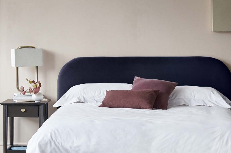 Neutral bedroom with a purple bed frame, white linen and simple furniture and accessories.