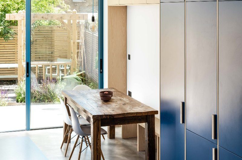 A dining area in the blue kitchen with a rustic table and simple chairs and benches.