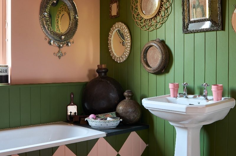 Bathroom with green panelling, flooring and a fitted tub with checkerboard style paint and vintage decor on the walls.