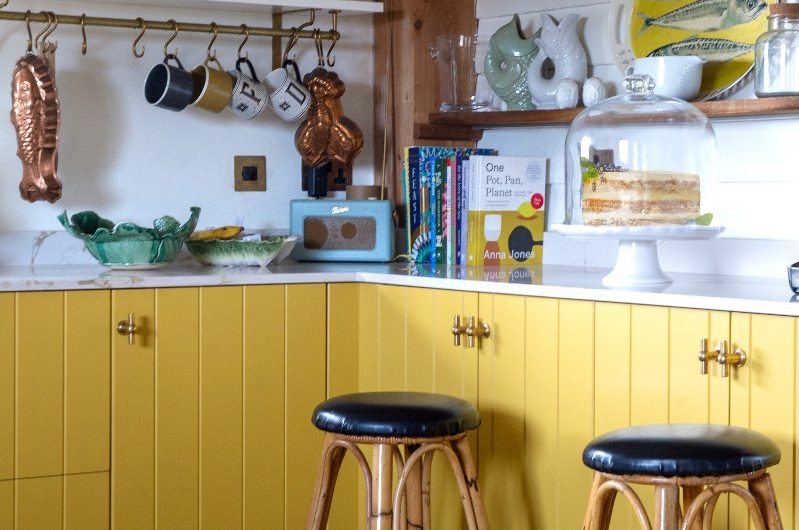 L-shaped cabinetry topped with white worktops, with wood open shelving decorated with quirky decor.