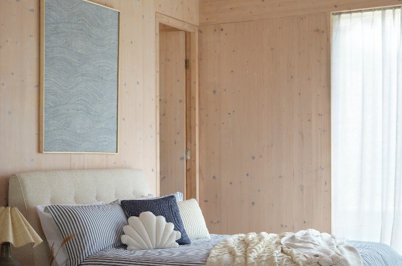 A wood drenched space with a neutral bed frame, blue and white striped bedding, and coastal-inspired decor.