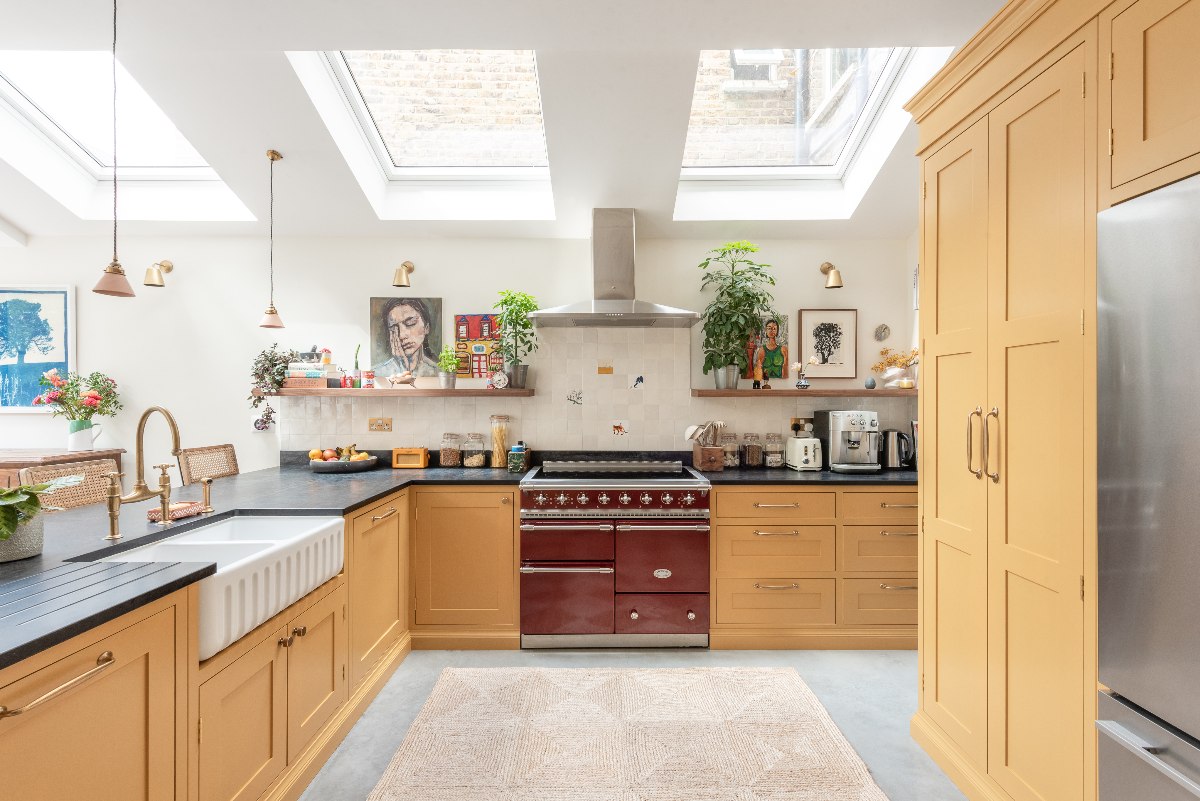 Mediterranean-inspired kitchen with an L-shaped layout, mustard yellow cabinetry, a burgundy range cooker and zellige tiles.