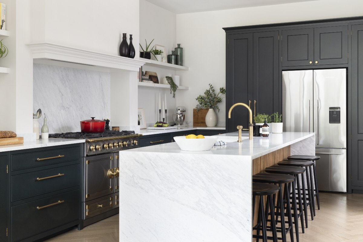 A Scandi kitchen with painted cabinetry, an island with stone surfaces, seating, and a sink and tap built in next to a cooking area with a range cooker.