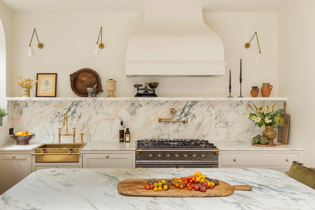 A contemporary kitchen design with marble surfaces, a marble shelf, gold sink and tap, and a classic range cooker.