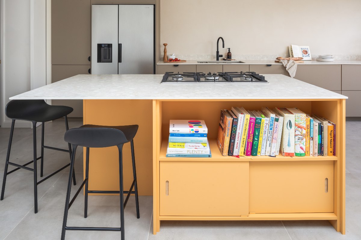 Grey run of kitchen cabinets with a yellow island with storage, hob and seating.